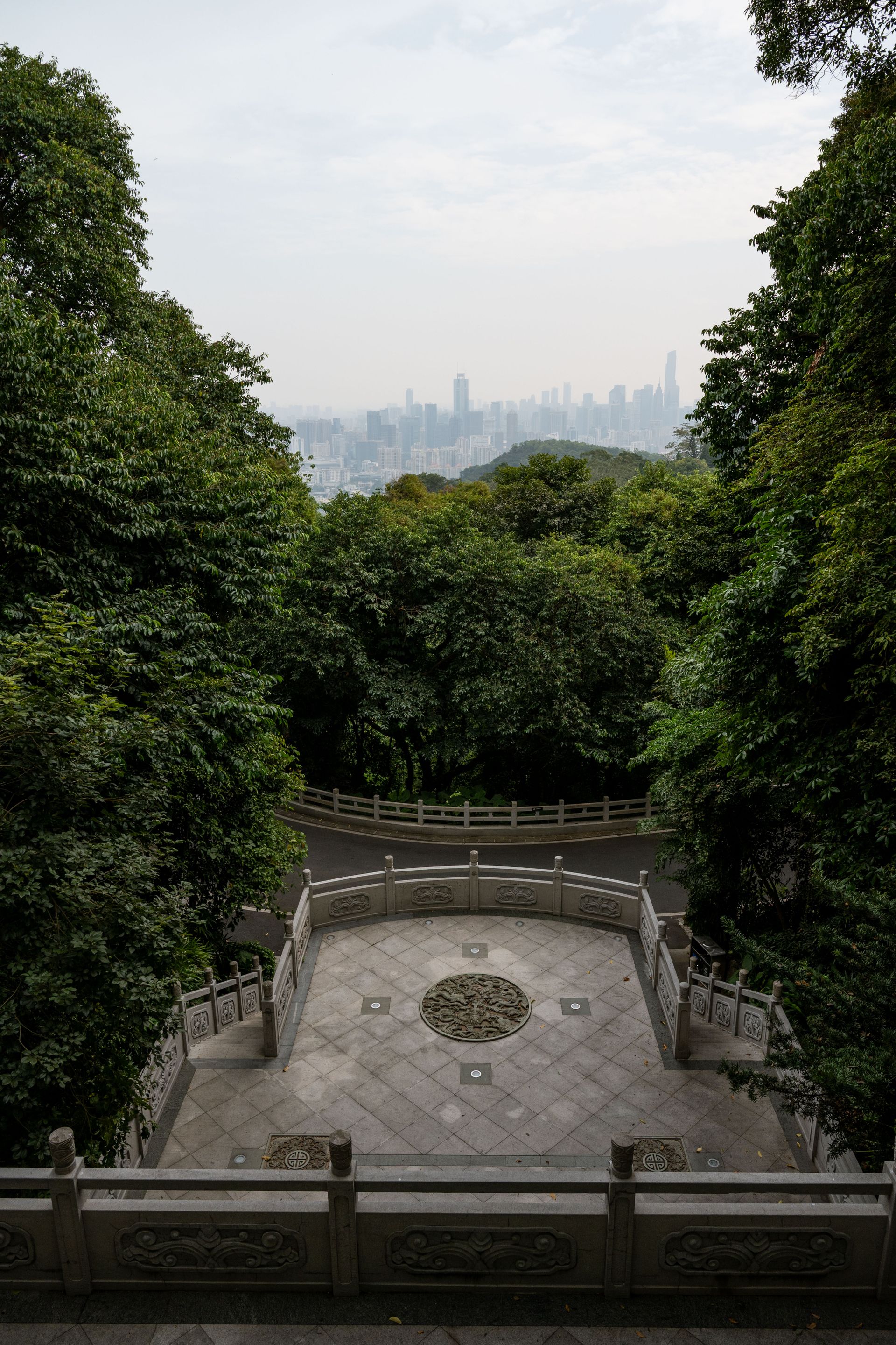 A peaceful stone observation deck surrounded by lush greenery with a view of Guangzhou skyline.