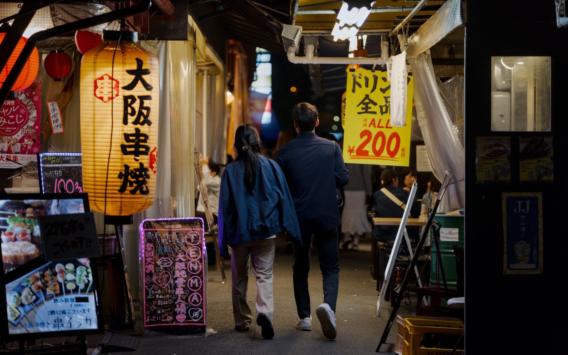 Couple walking in lively Osaka night market with illuminated signs and lanterns.
