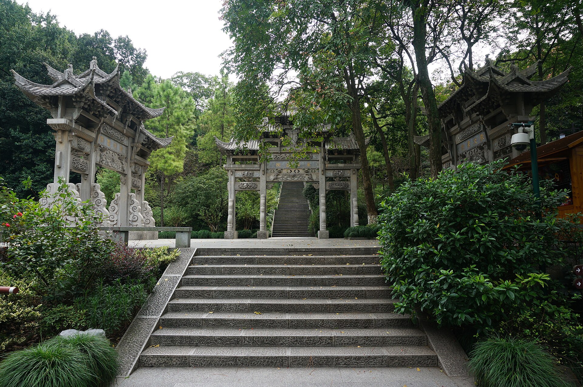 三座石牌坊在松柏林间对称立着，额枋上刻着纹样但无可辨字迹，中央一座后接向上延伸的长条石阶