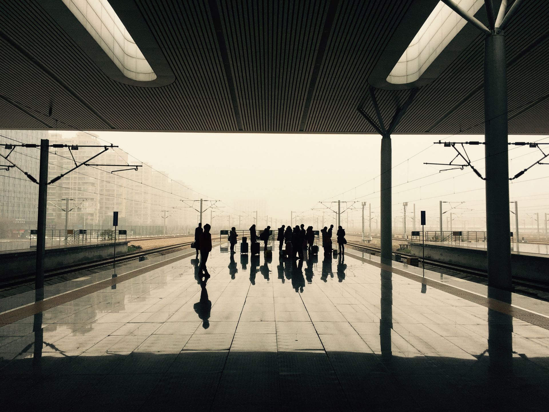 Silhouetted travelers await a train at a contemporary station with sleek architecture.