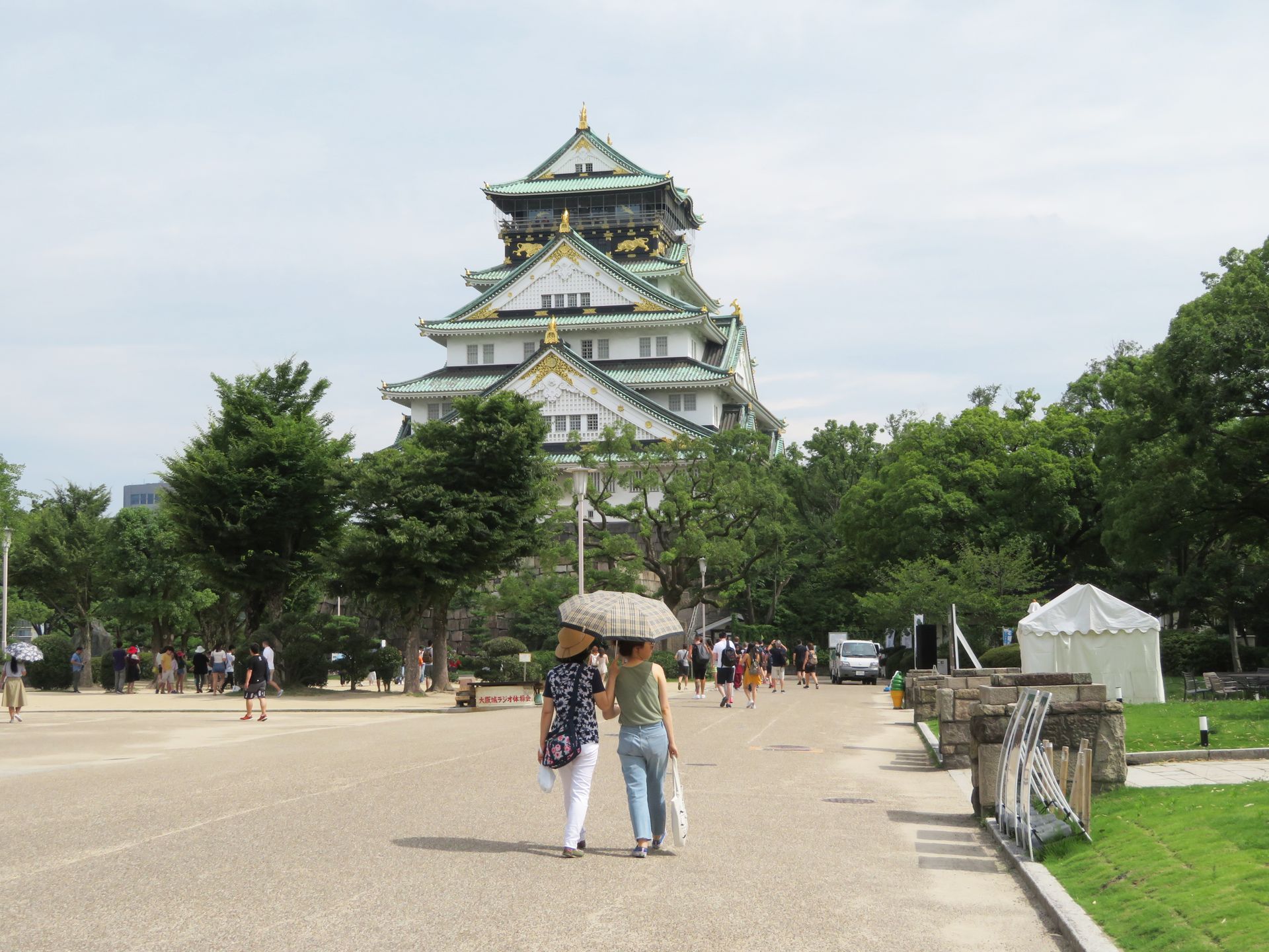 Visitors with umbrellas walking towards Osaka Castle, Osaka, Japan, on a bright summer day.