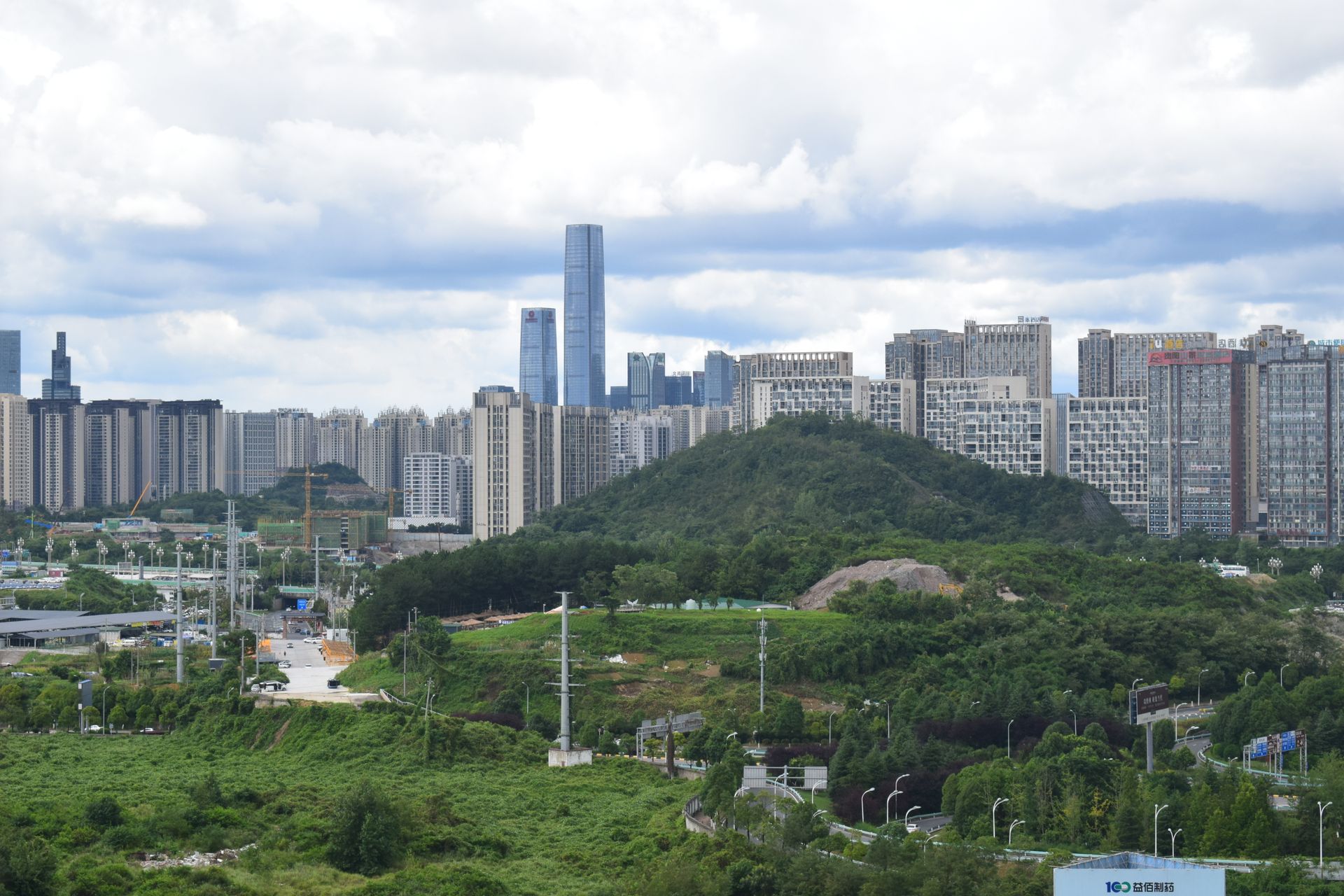 A city skyline merges with nature, featuring skyscrapers behind lush green hills.