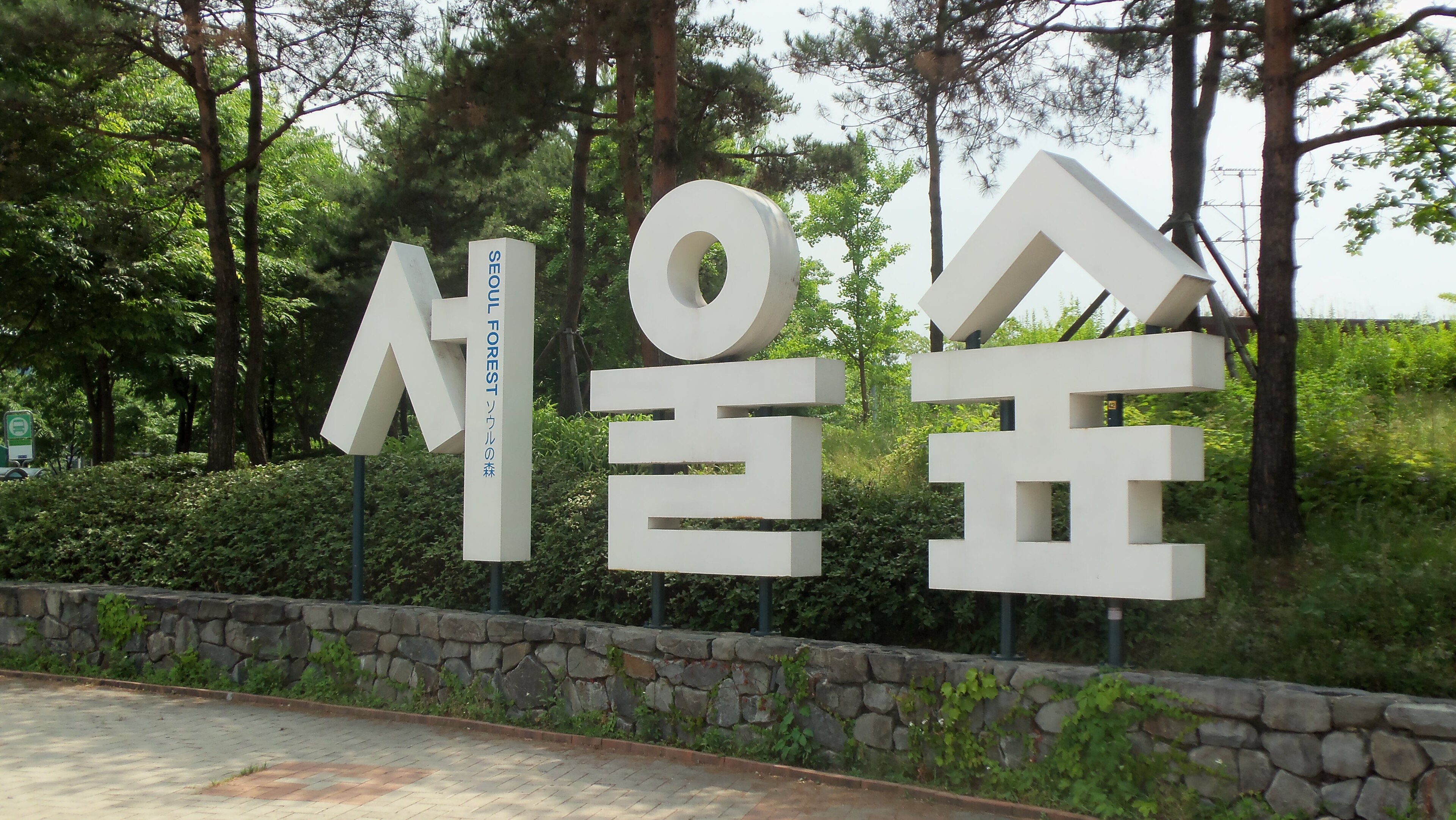 首尔森林的石墙步道，白色标识牌上写有「서울숲 / SEOUL FOREST」