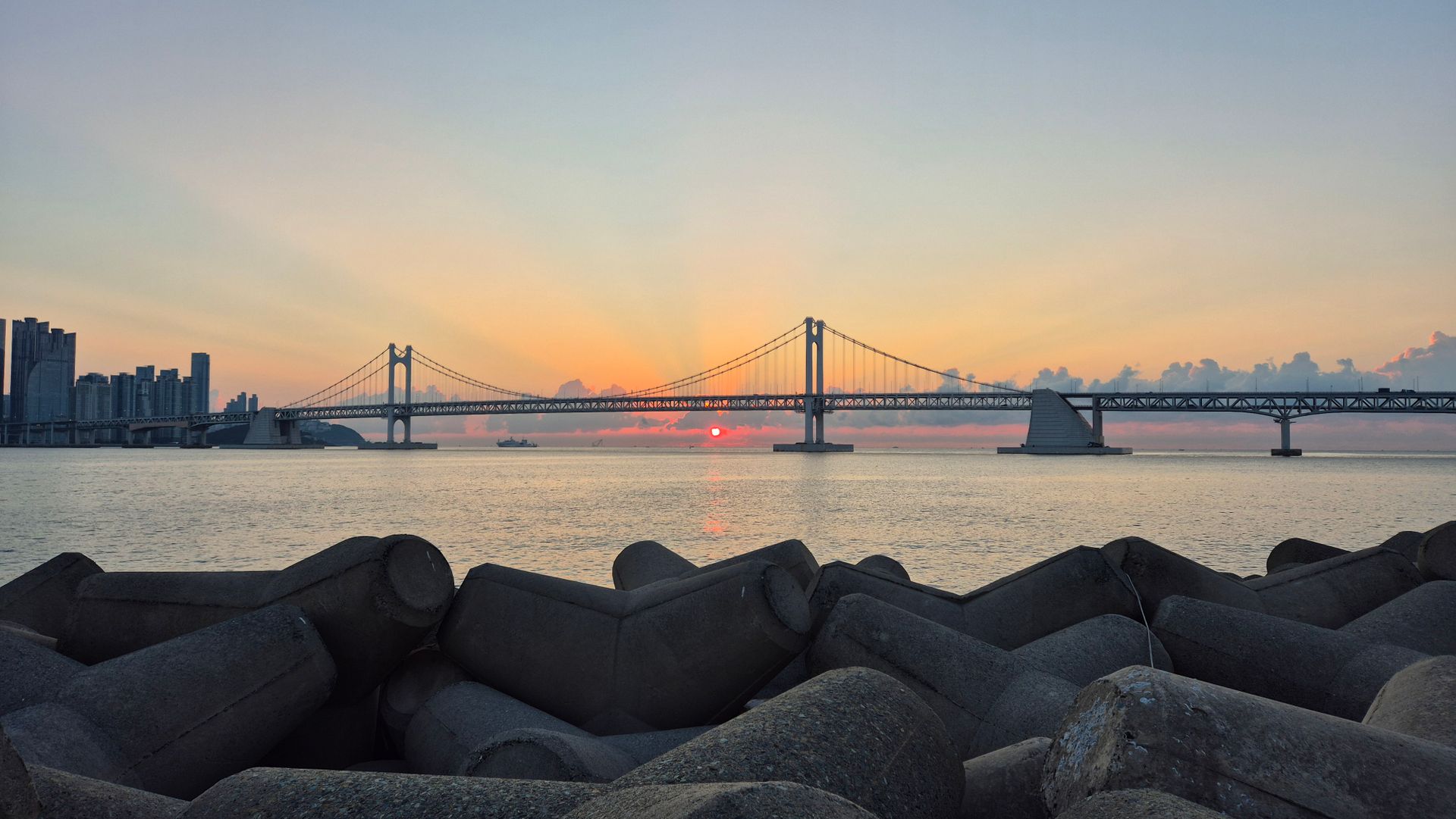 Scenic view of Gwangandaegyo Bridge in Busan at sunset with calm sea and cityscape.