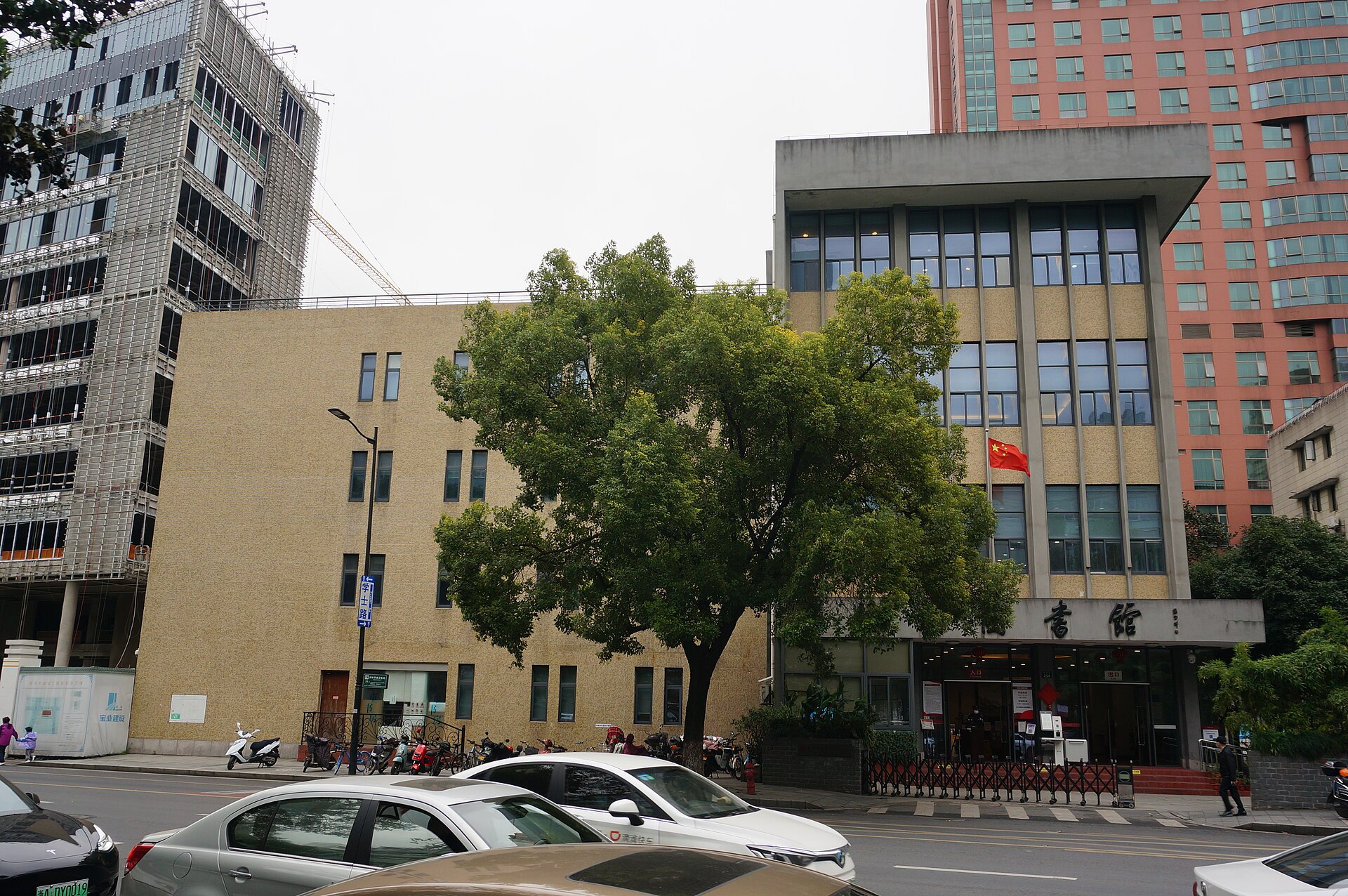 浣纱路上的杭州图书馆旧馆临街外观：浅黄色外墙的多层建筑，入口上方有图书馆标识并悬挂国旗，门前是行道树与浣纱路街面。