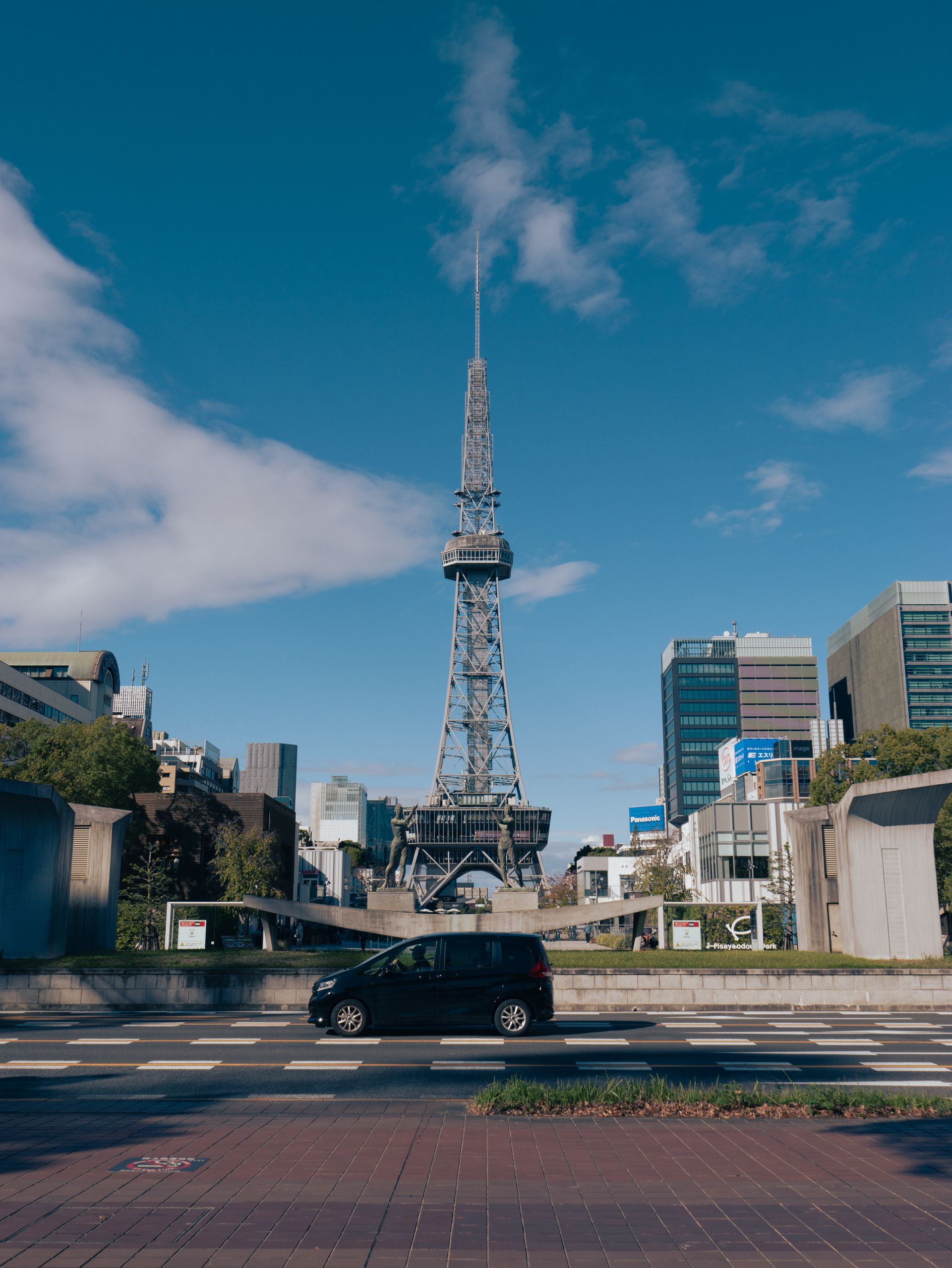 A view of Nagoya TV Tower surrounded by urban buildings under a clear blue sky.