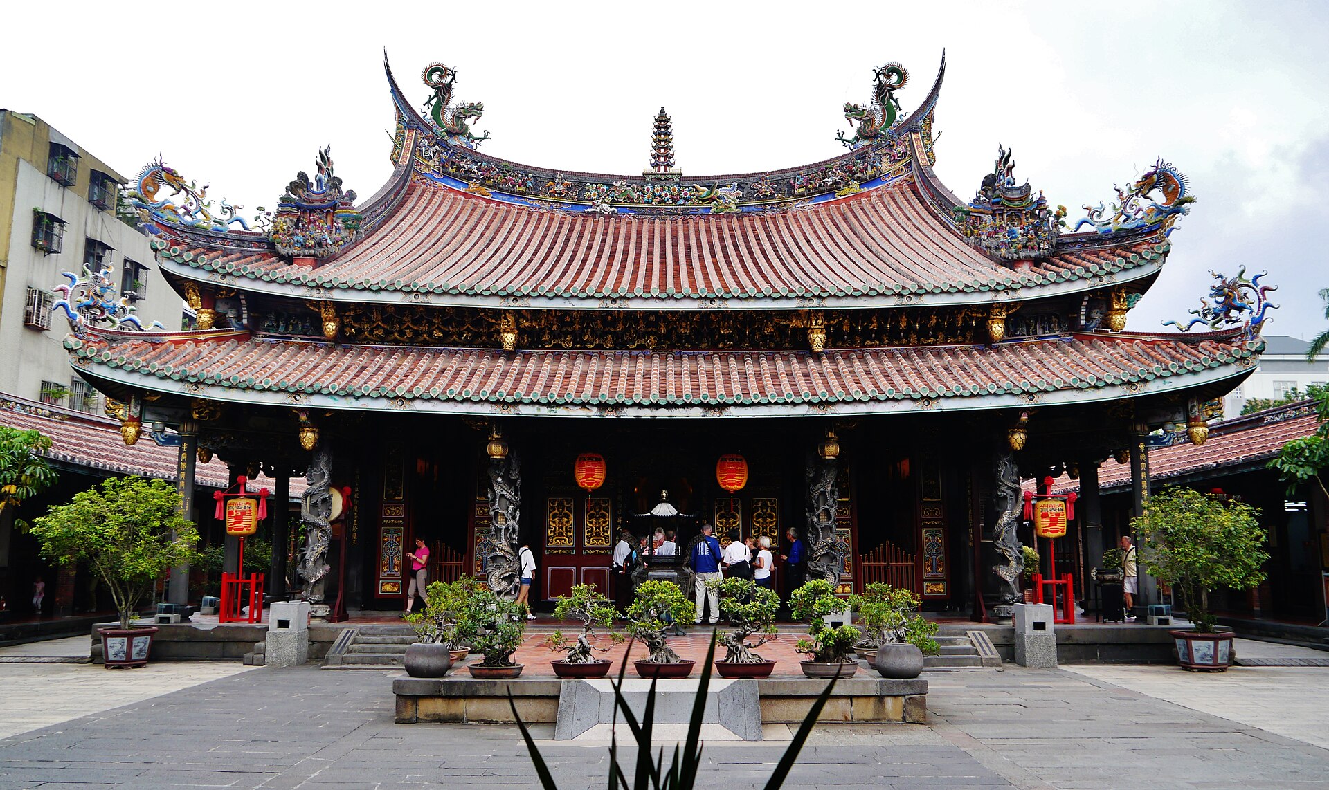 庙宇重檐屋顶上饰着彩色龙兽，檐下斗拱彩绘，正门三开间前立着石狮与台阶，庭院里对称摆着盆景