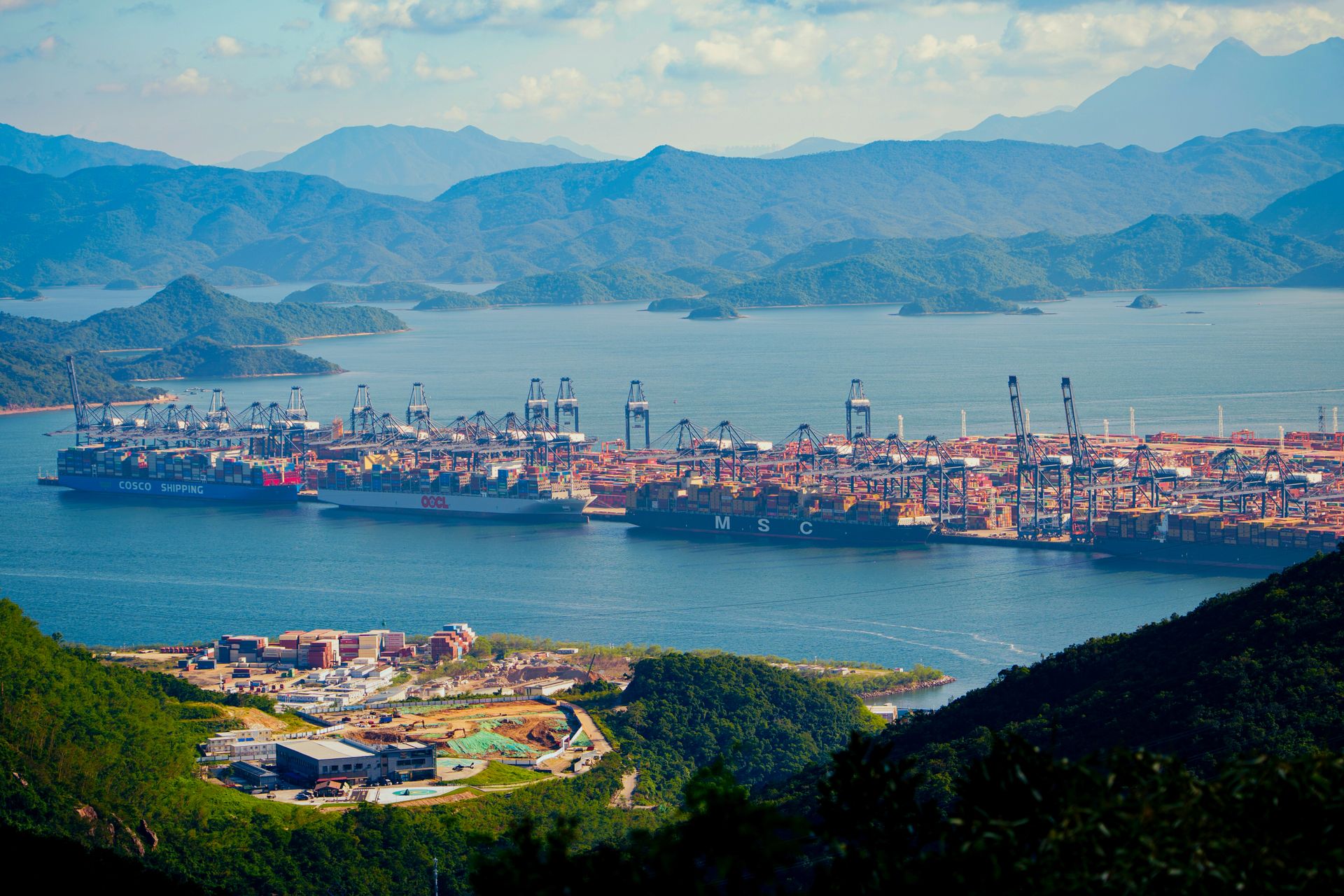 Aerial shot of a bustling shipping port amidst mountains by the water, showcasing international trade.