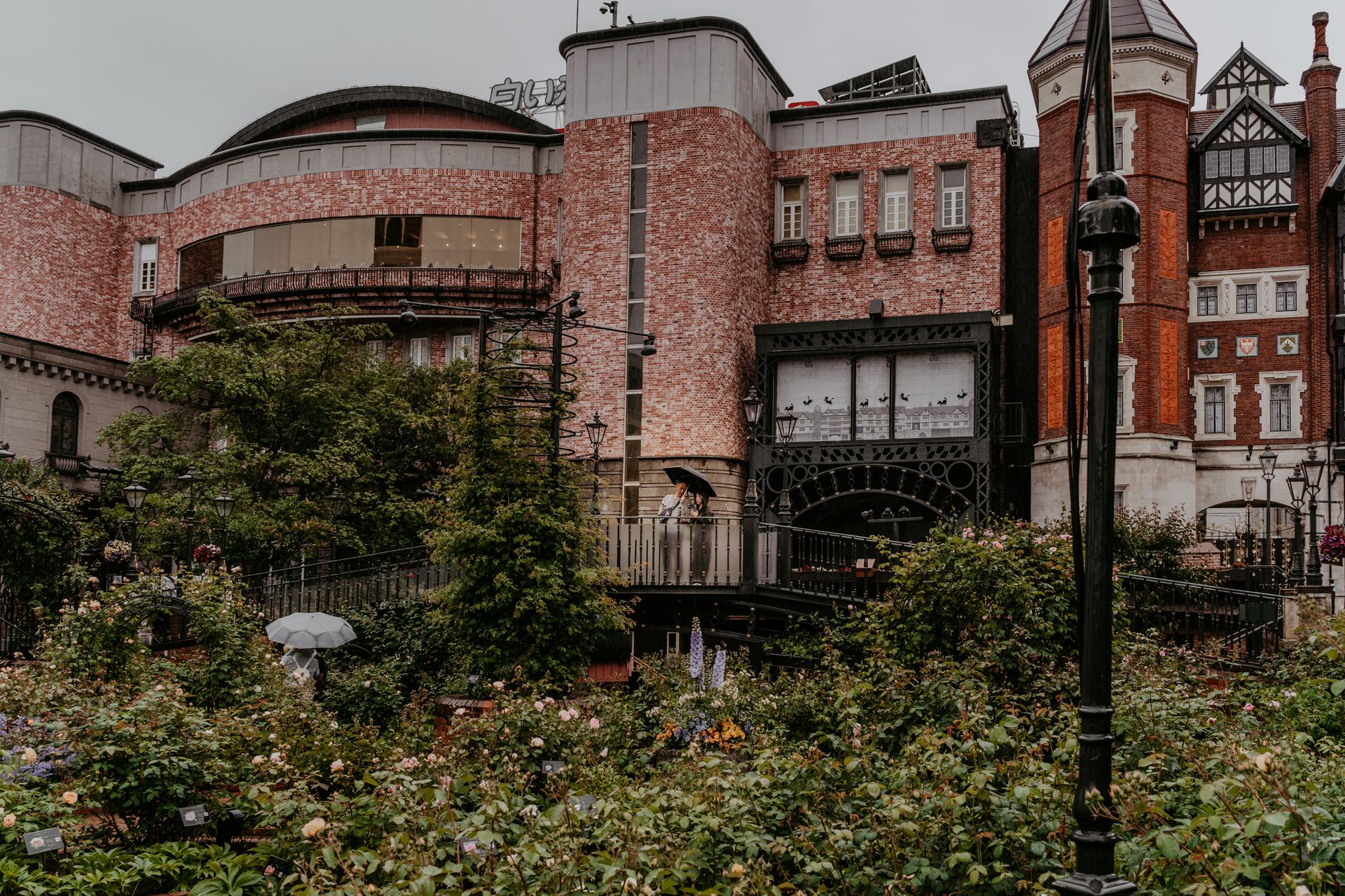 A brick building with garden in Sapporo, Japan. People with umbrellas on a rainy day.