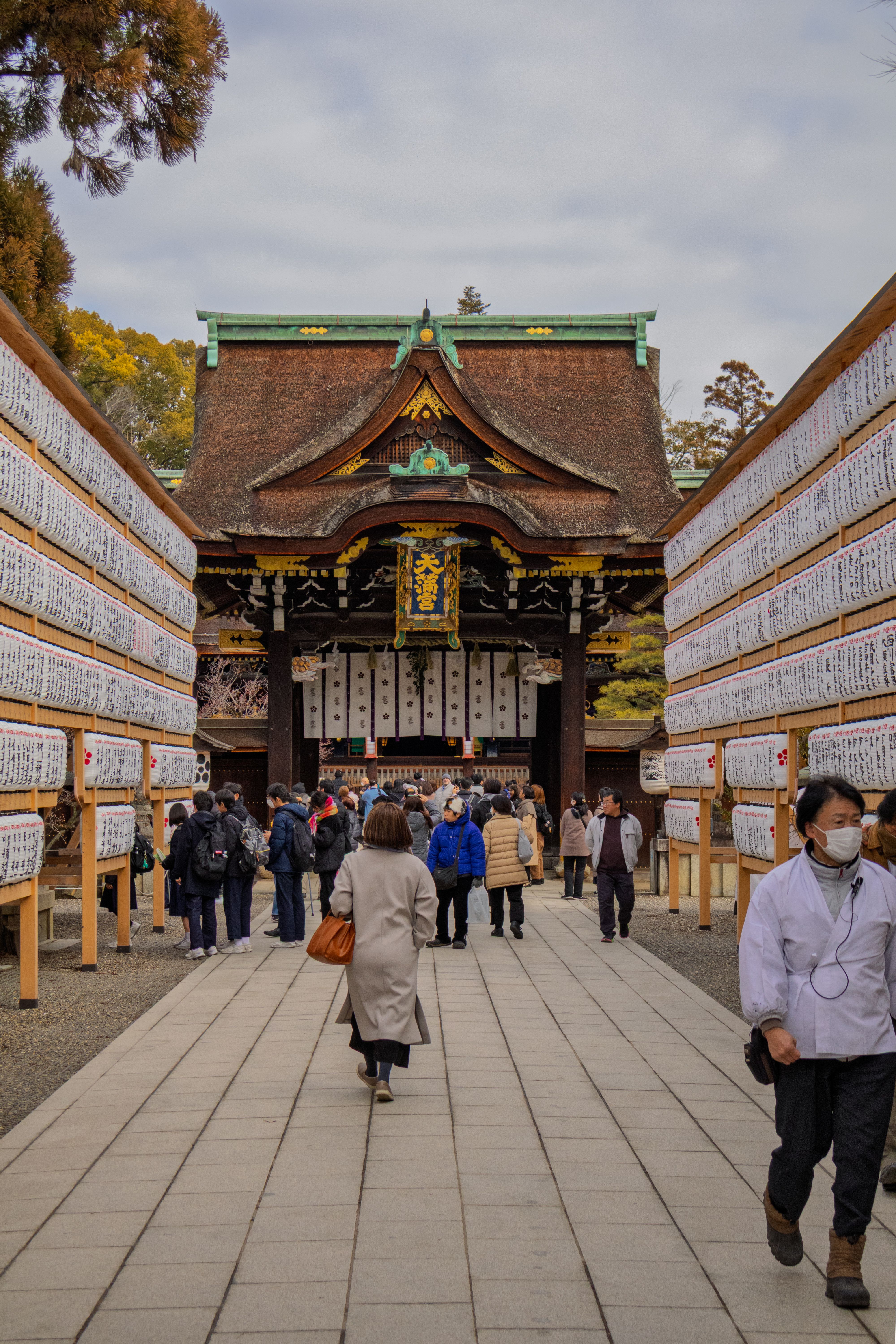 楼门檐下挂着金边蓝底竖匾「天満宮」，参道两侧木架上悬满白色纸片排成通道，门前来往的人不少
