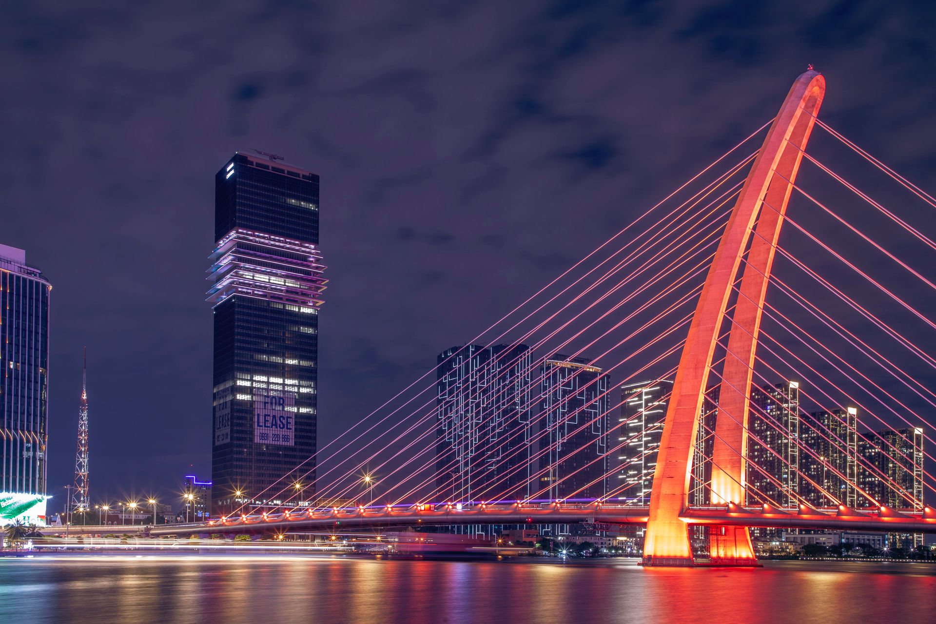 Stunning nighttime view of a modern suspension bridge illuminated with vibrant lights over a city river.