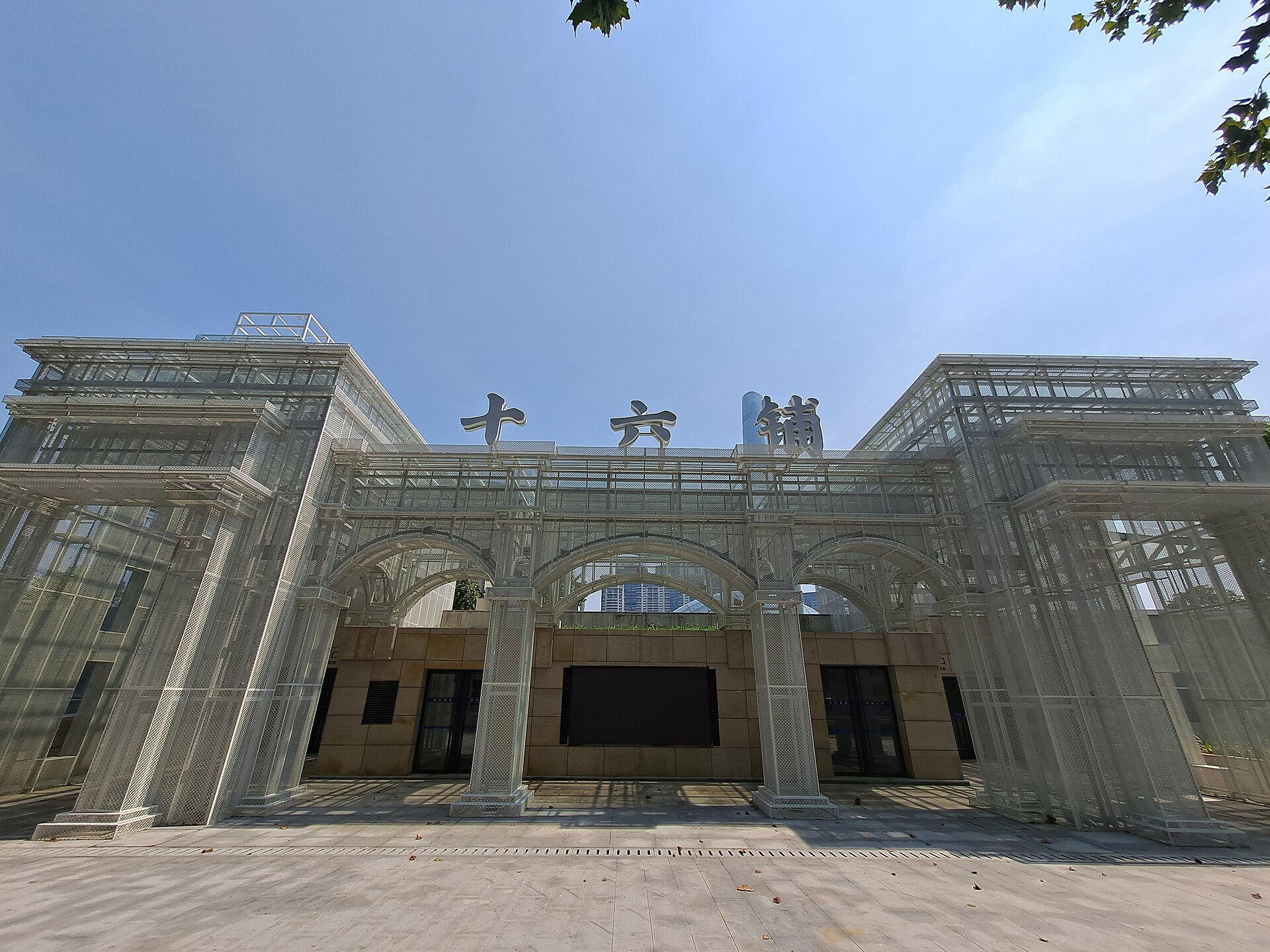 白色金属网格搭成的三拱门楼，横梁上立着「十六铺」三个大字，拱门后露出米色石墙与高层楼宇