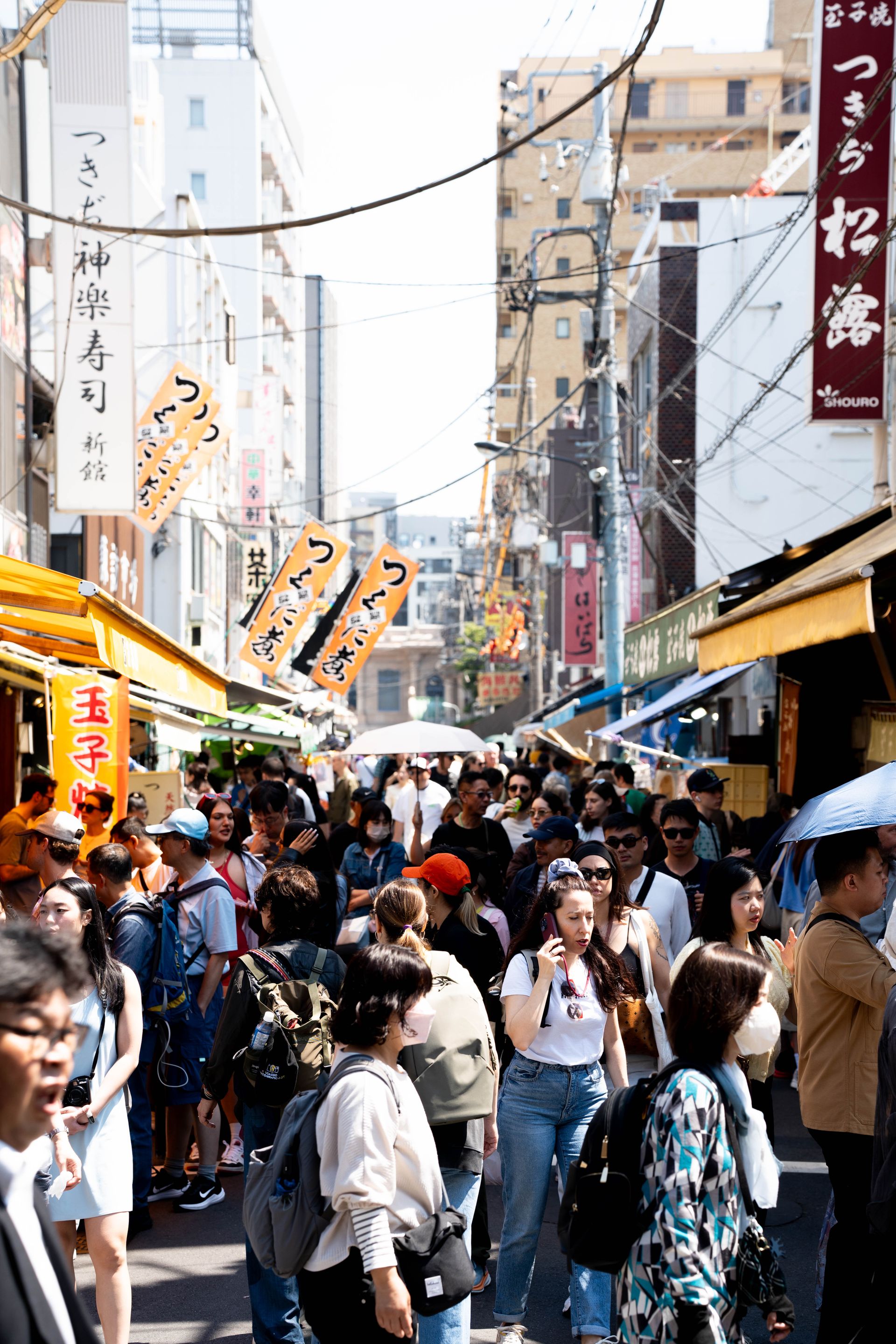 Crowded street market scene in Tokyo, vibrant energy with diverse people shopping under sunny skies.