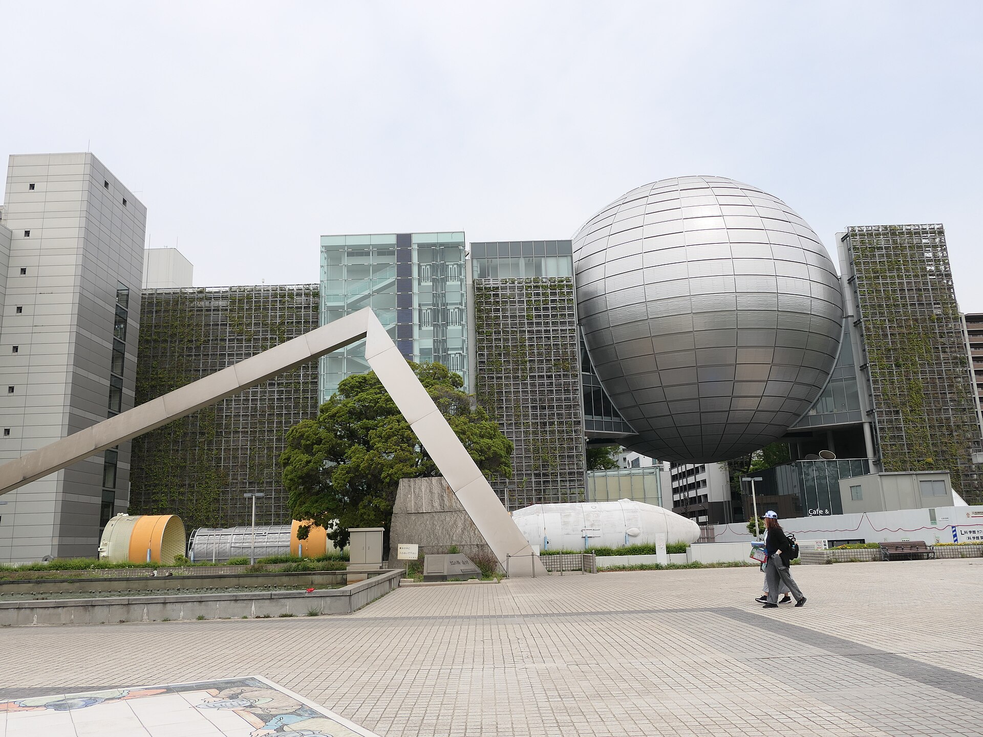 银灰色大球嵌在楼体之间，两侧方楼外墙覆满绿色植被格栅，球下的玻璃入口开着