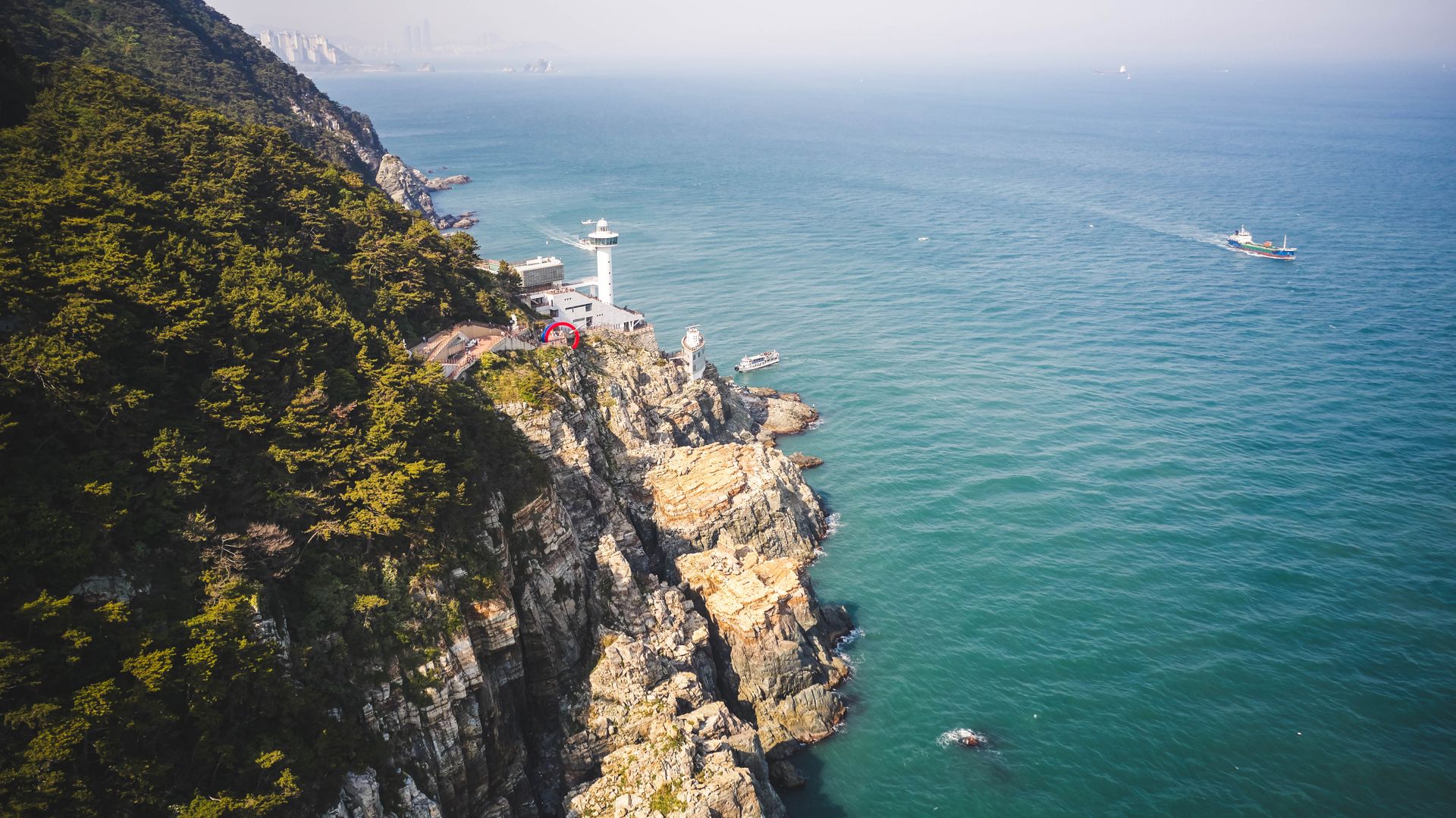 A breathtaking aerial shot of Yeongdo Lighthouse against a rocky cliff by the ocean.