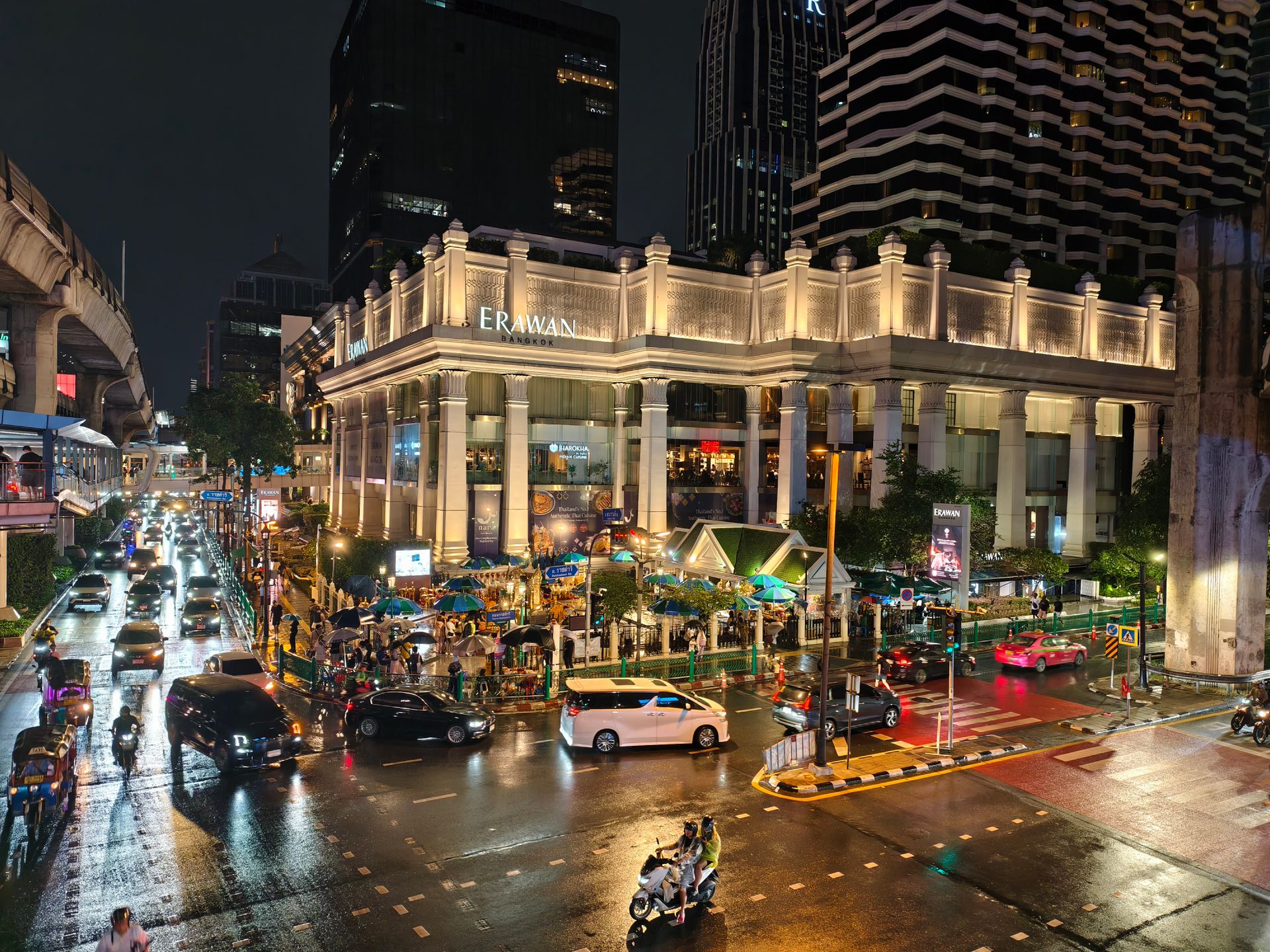 Vibrant street scene at night near Erawan Bangkok, showcasing urban life, traffic, and illuminated architecture.