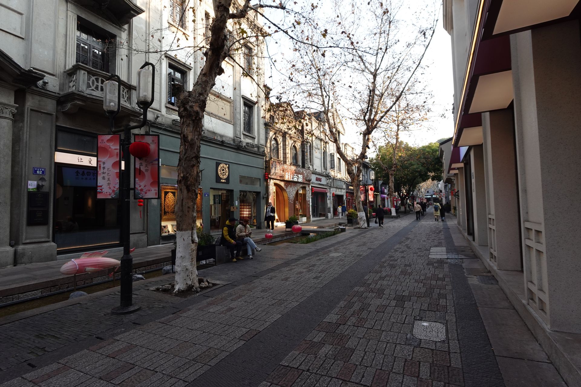 A picturesque street in Hangzhou, China, with historic architecture and red lanterns lining the sidewalk on a quiet afternoon.
