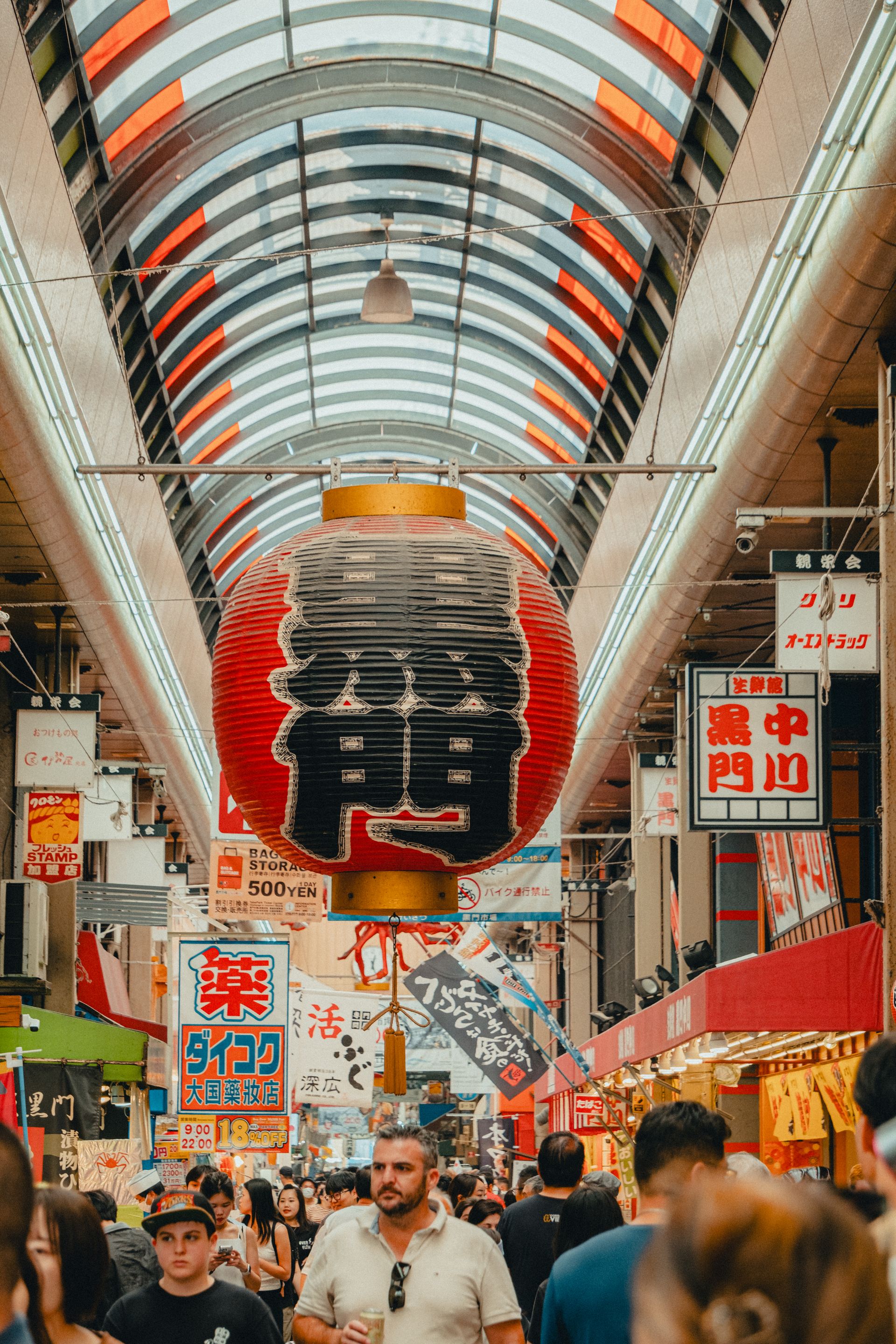Bustling shopping street in Osaka with vibrant lanterns and crowded atmosphere.